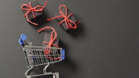 Three-black-gifts-tied-with-red-string-and-shopping-cart-on-black-background-with-copy-space