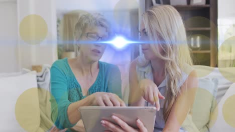Animation-of-light-spots-and-trails-over-caucasian-woman-and-her-adult-daughter-using-tablet