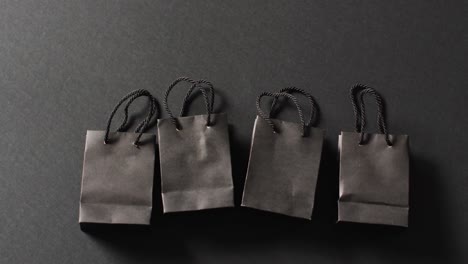 Vier-Schwarze-Geschenktüten-Mit-Schwarzen-Griffen-In-Einer-Reihe-Auf-Dunkelgrauem-Hintergrund-Mit-Kopierraum