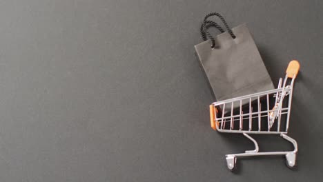 Black-gift-bag-in-shopping-trolley-on-black-background-with-copy-space