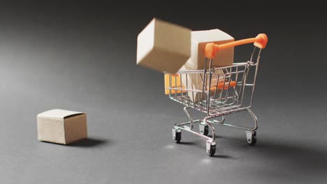 Shopping-trolley-spilling-with-cardboard-boxes,-on-seamless,-lit-black-background-with-copy-space