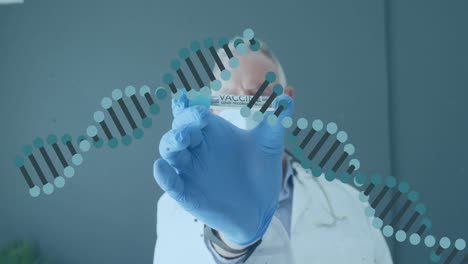 Animation-of-dna-strands-over-caucasian-male-doctor-wearing-face-mask-holding-tube-with-vaccine