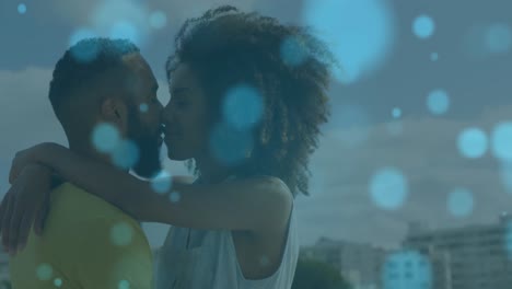 Animation-of-light-spots-over-african-american-couple-embracing-and-kissing-at-beach