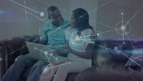 Animation-of-network-of-connections-with-light-trails-over-african-american-couple-using-laptop