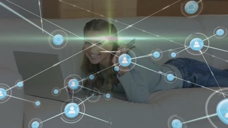 Animation-of-network-of-connections-with-icons-over-caucasian-woman-using-laptop