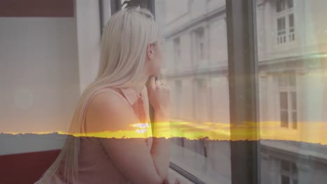 Animation-of-sunset-over-thoughtful-smiling-caucasian-woman-looking-out-of-window-in-office