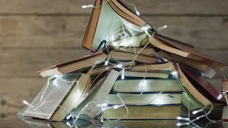 Video-of-christmas-fairy-lights-and-stack-of-books-on-wooden-background