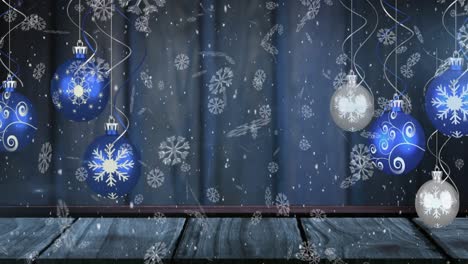 Animation-of-snow-falling-over-christmas-baubles-on-blue-background