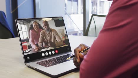 African-american-man-using-laptop-for-video-call,-with-diverse-business-colleagues-on-screen