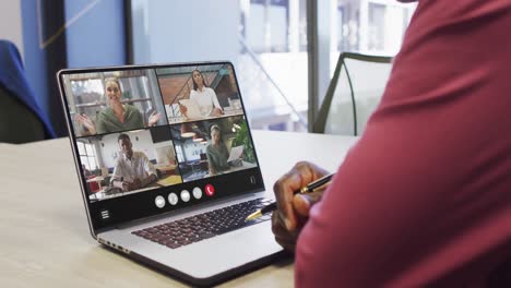 African-american-man-using-laptop-for-video-call,-with-diverse-business-colleagues-on-screen