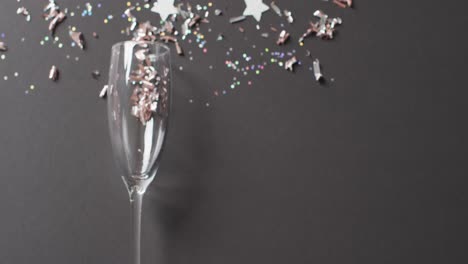 Video-of-champagne-flute-glass,-with-glitter-confetti-and-silver-stars-on-black,-with-copy-space