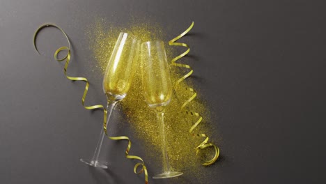 Video-Von-Zwei-Champagnergläsern-Mit-Goldenen-Luftschlangen-Und-Glitzer-Auf-Schwarz,-Mit-Kopierraum