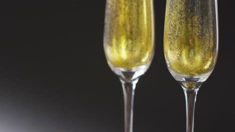 Video-of-two-full-champagne-flute-glasses-on-black-background,-with-copy-space