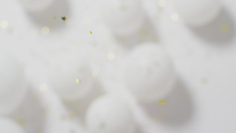 Video-of-gold-confetti-falling-over-defocussed-white-balloons-on-white-background