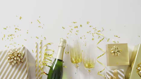Video-Von-Champagnerflaschen,-Gläsern-Und-Geschenken-Mit-Goldenen-Luftschlangen-Und-Konfetti-Auf-Weiß