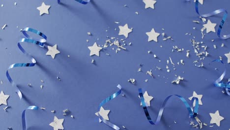 Video-of-multiple-silver-stars-and-party-streamers-scattered-on-blue-background