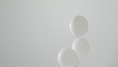 Video-of-three-white-balloons-on-white-strings-floating-on-white-background,-with-copy-space