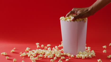 Video-of-close-up-of-hand-and-popcorn-on-red-background