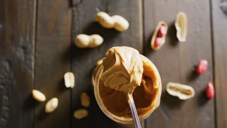 Video-of-close-up-of-peanut-butter-and-peanuts-on-wooden-background