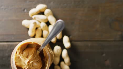 Video-of-close-up-of-peanut-butter-and-peanuts-on-wooden-background