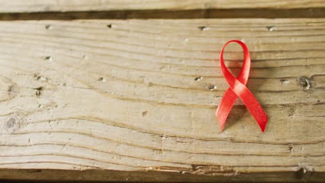 Video-of-close-up-of-red-cancer-ribbon-on-wooden-background