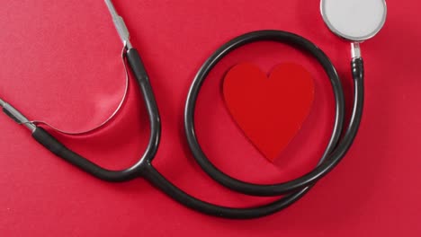 Video-of-close-up-of-heart-and-stethoscope-on-red-background