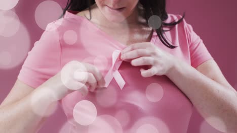 Animation-of-light-spots-over-caucasian-woman-with-pink-ribbon-on-pink-background