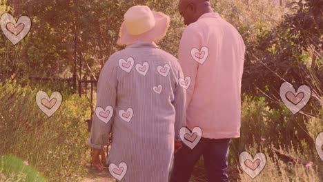 Animation-of-hearts-over-senior-african-american-couple-walking-in-garden-at-christmas
