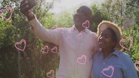 Animation-of-hearts-over-senior-african-american-couple-taking-selfie-at-christmas