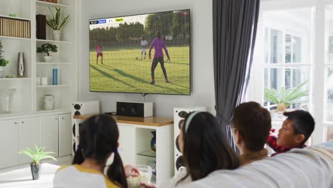 Asian-family-watching-tv-with-diverse-male-soccer-players-playing-match-on-screen
