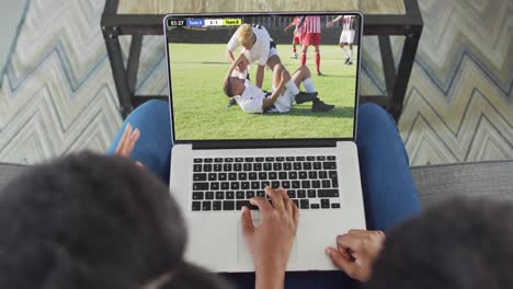 Video-of-african-american-couple-sitting-on-sofa-and-watching-football-on-laptop-at-home