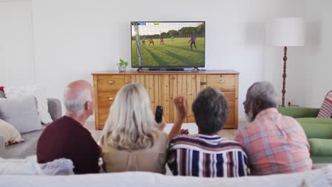 Diverse-senior-couples-watching-tv-with-diverse-male-soccer-players-playing-match-on-screen