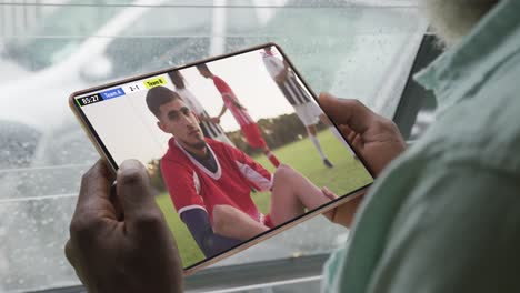 African-american-man-using-tablet-with-diverse-male-soccer-players-playing-match-on-screen
