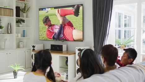 Video-Eines-Asiatischen-Paares-Mit-Sohn-Und-Tochter,-Die-Auf-Dem-Sofa-Sitzen-Und-Zu-Hause-Fußball-Schauen
