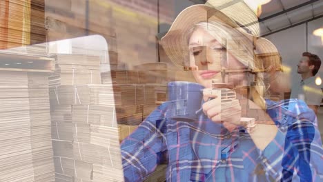 Animation-of-caucasian-woman-drinking-coffee-and-using-laptop-over-supervisor-inspecting-inventory