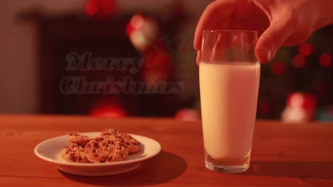 Animation-of-merry-christmas-text-over-hand-with-cookies-and-milk