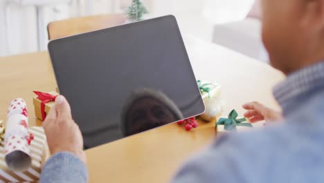 Video-of-senior-biracial-man-holding-gift-making-christmas-tablet-video-call,-copy-space-on-screen