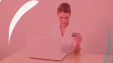 Animation-of-shapes-over-caucasian-woman-using-laptop-and-holding-credit-card-for-online-shopping