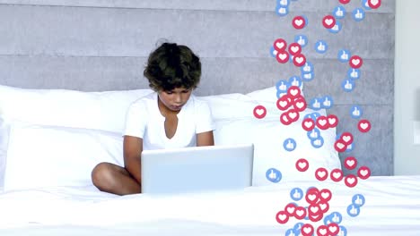 Animation-of-like-and-heart-icons-floating-over-biracial-girl-using-laptop-on-the-bed