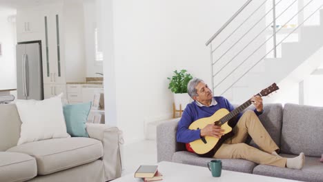 Video-Eines-älteren-Gemischtrassigen-Mannes,-Der-Zu-Hause-Auf-Der-Couch-Singt-Und-Akustikgitarre-Spielt