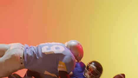 Video-of-diverse-american-football-players-tackling-with-ball-over-yellow-to-orange-background
