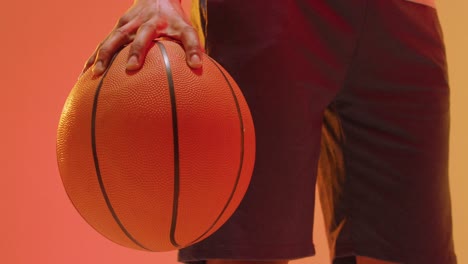 Video-Des-Mittelteils-Eines-Gemischtrassigen-Männlichen-Basketballspielers-Mit-Ball-Auf-Orangefarbenem-Bis-Gelbem-Hintergrund