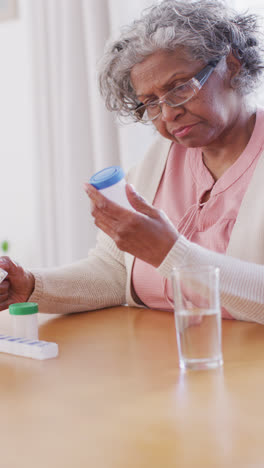 Vertical-video-of-senior-african-american-woman-sitting-at-table,-taking-pills
