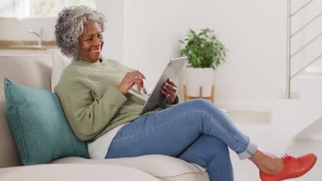 Portrait-of-happy-senior-african-american-woman-sitting-on-sofa,-using-tablet