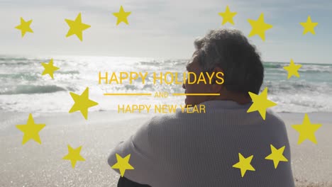 Animation-of-happy-holidays-and-happy-new-year-text-with-stars-over-senior-biracial-man-at-beach