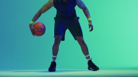 Video-of-biracial-male-basketball-player-bouncing-ball-on-green-to-blue-background