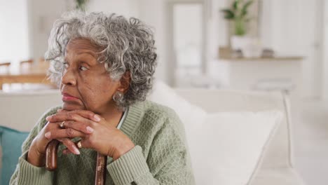 Porträt-Einer-Glücklichen-älteren-Afroamerikanischen-Frau,-Die-Auf-Dem-Sofa-Sitzt-Und-Sich-Auf-Einen-Gehstock-Stützt