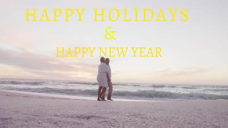 Animation-of-happy-holidays-and-happy-new-year-text-over-senior-biracial-couple-at-beach