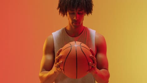 Video-of-biracial-male-basketball-player-with-ball-on-orange-to-yellow-background