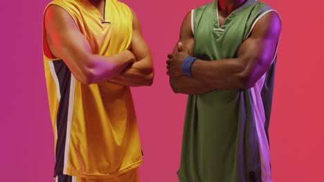 Video-of-portrait-of-two-diverse-male-basketball-players-with-arms-crossed-on-pink-background